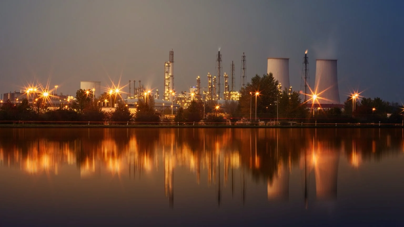 Refinery lit up at dusk, reflected in water